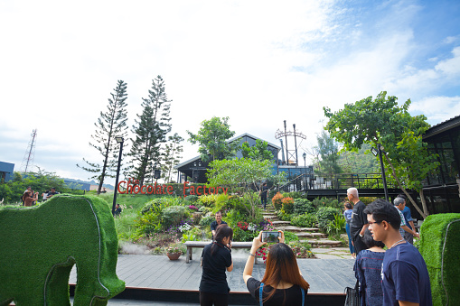 Thai people are visiting Chocolate Factory coffee shop in Khao Yai landscape in valley in Nakhon Ratchasima. A woman is taking photos, a man is standing close by. In background are more people