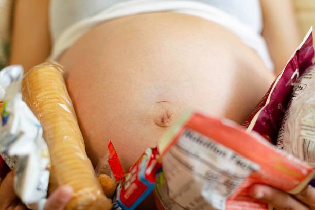 A hungry pregnant woman eating snacks. Pregnancy cravings. A pregnant woman holding many snacks and food cravings around her baby belly. family eating potato chips stock pictures, royalty-free photos & images