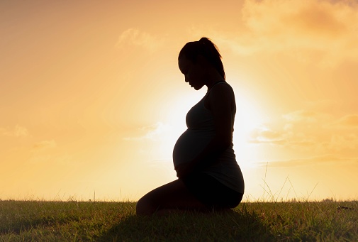 Young Asian pregnant woman sitting on couch drinking pure fresh glass of water in the morning at home. Happy healthy lifestyle.