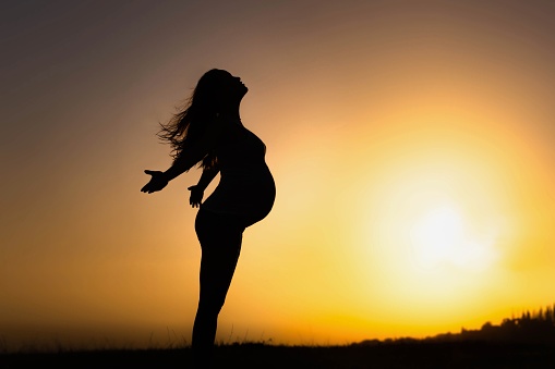 A carefree pregnant woman with her arms out in front of a sunrise.