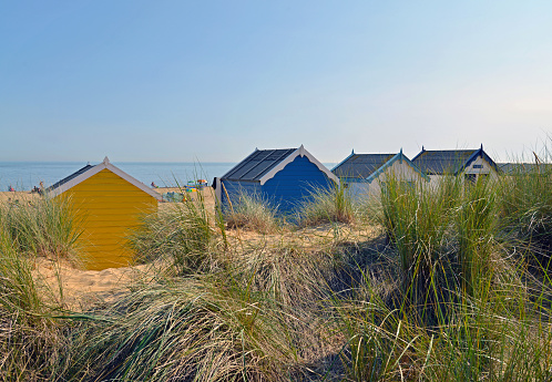 Colorful beach huts nestled among the sand dunes on a beach in Southwold in Suffolk on the east coast of England. Lots of copy space this image. The people are totally unrecognizable.