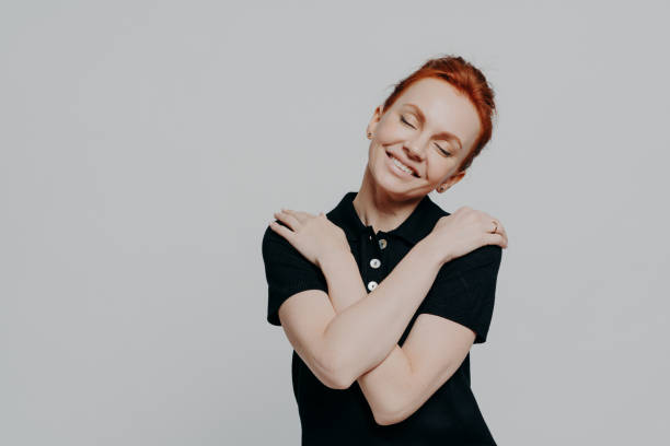 istock Happy red-haired woman with closed eyes dressed casually hugging herself gently and tilting head 1336930624