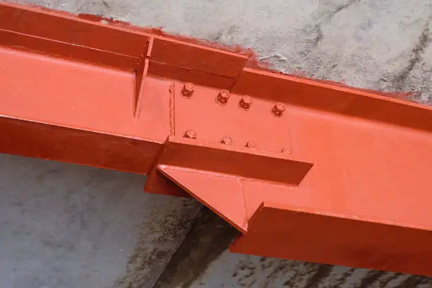 Photo of Bolted connection of steel beams. Metal construction covered primer red iron oxide.