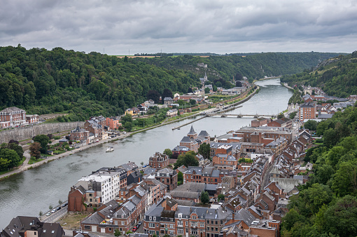 Dinant, Wallonia, Belgium - August 8, 2021: Citadel Fort. Aerial view downstream Meuse with cityscape on both sides of river under heavy rainy cloudscape.