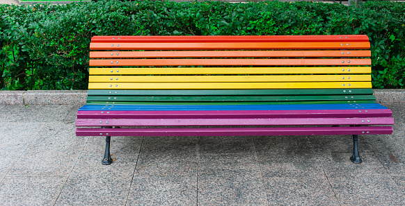 A street bench painted in rainbow colors. With no one sitting, waiting to be used. Concept of pride, acceptance, naturalness