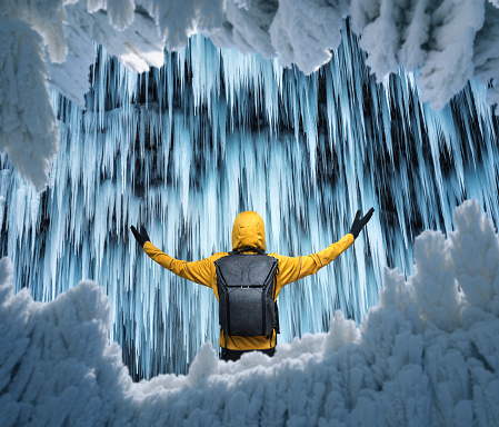 Man in a yellow jacket watching a spectacular frozen waterfall. View through the ice.