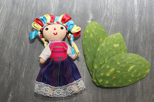 Festive Mexican objects: handmade doll and tricolor tie bow next to nopales