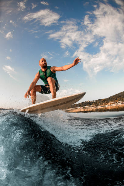 istock sportsman on wakeboard while skilfully jumping over splashing river wave against blue sky. 1336949440