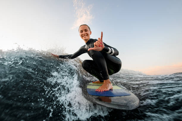 mujer sonriente se sienta en la tabla de wakesurf y monta la ola y toca las olas con una mano - surf fotografías e imágenes de stock