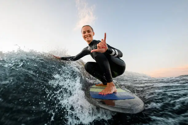 smiling woman in wetsuit sits on wakesurf board and rides the wave and touches the waves with one hand