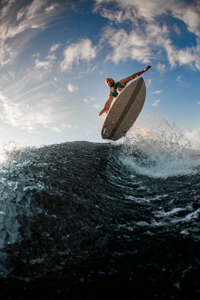 красивый вид снизу на мужчину-вейкбордиера во время прыжка через плещущиеся волны - wakeboarding waterskiing water ski sunset стоковые фото и изображения
