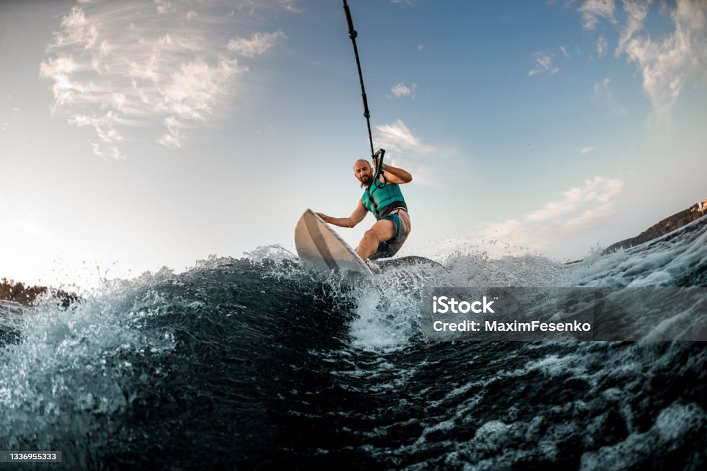 man holds rope and catches a wave on wakesurf. Wakesurfing on the river. energetic sports man holds rope and catches a wave on wakesurf. Wakesurfing on the river. Summertime leisure Wakesurfing Stock Photo