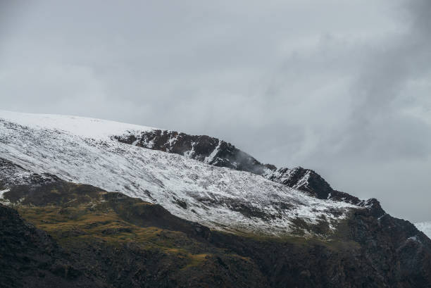 istock Minimalist highlands landscape with snow-capped mountains under cloudy sky. Snowbound high mountain range in overcast weather. Atmospheric minimalism with green mountains, white snow and gray sky. 1336961775