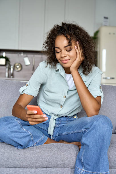istock Serene mixed race relaxed student girl sit on sofa at home holding cellphone. 1336961961