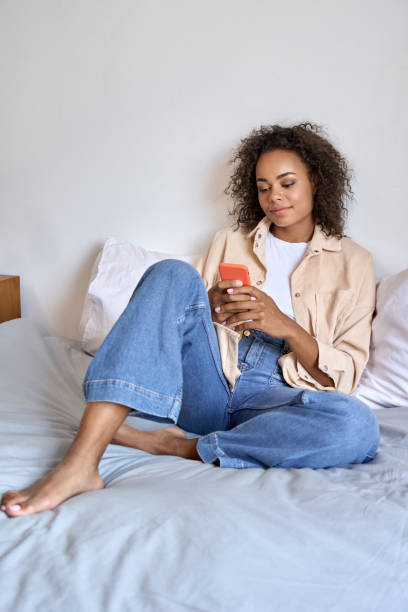 istock Young happy afro American mixed race girl using cell phone sit on bed relaxed. 1336961972