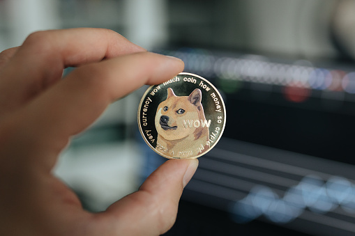 Dogecoin meme coin. Cryptocurrency physical coin close-up, held between two fingers