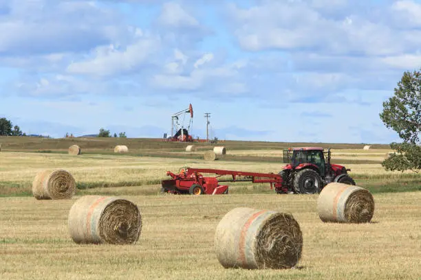 Scenic of hay bales,hay baler equipment, with oil and gas Pumper in background.  Prairie scene.