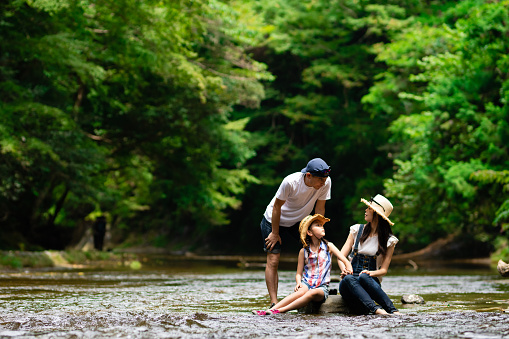 Father, mother and daughter sitting on a rock in a mountain stream and talking