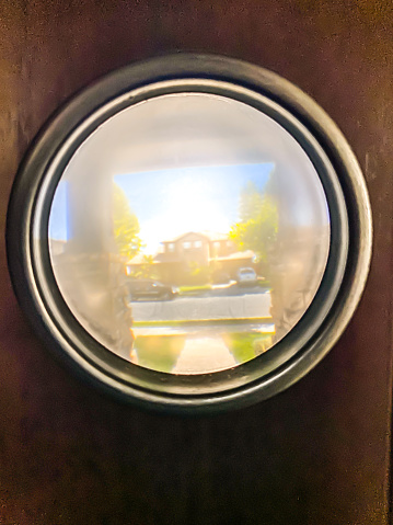 June 12, 2021. California. The lens of a camera is looking out into a neighborhood through a peephole.  This peephole reflects a bright sunny neighborhood and the first look of possible delivery packages or visitors.