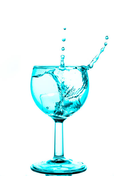 istock Interesting splash pattern with lines of droplets created by dropping an ice cube into a wine glass of clear liquid highlighted with a aque lighting effect and isolated against a white background. 1336983879