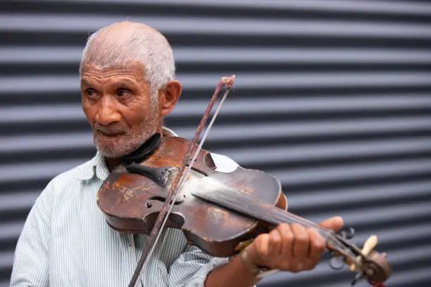 Close up photo of a senior adult musician gray-hair man playing the violin outdoors and turned his head to the side is looking pensively into the distance. High quality photo