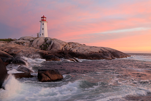 Peggy’s Cove Lighthouse illuminated at sunset with dramatic waves on the foreground, Nova Scotia, Canada