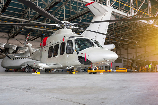 Passenger helicopter and airplanes in the hangar. Rotorcraft and aircrafts under maintenance. Checking mechanical systems for flight operations