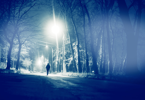 Woman walking alone on path in mystic forest . Illuminated way in the dark forest