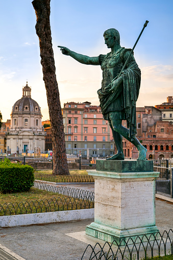 The first light of the evening envelops the statue of the Emperor Gaius Iulius Caesar Augustus, also know as Octavian or Augustus, along the Fori Imperiali boulevard, in the ancient and imperial heart of Rome. This bronze statue, placed in front of the Trajan's Forum, is a copy of the marble original currently preserved in the Vatican Museums. Caesar Augustus was the first Roman emperor, revered as father of the homeland (Patri Patriae) and artecife of a long period of domination, prosperity and peace throughout the empire, known as Pax Romana. In the background the Forum of Trajan and the baroque dome of the church of the Santissimo Nome di Maria. In 1980 the historic center of Rome was declared a World Heritage Site by Unesco. Image in high definition format.