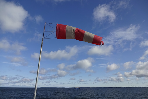 Close up of red and white windsock indicator on blue sky with many white clouds background. Navy sea water.