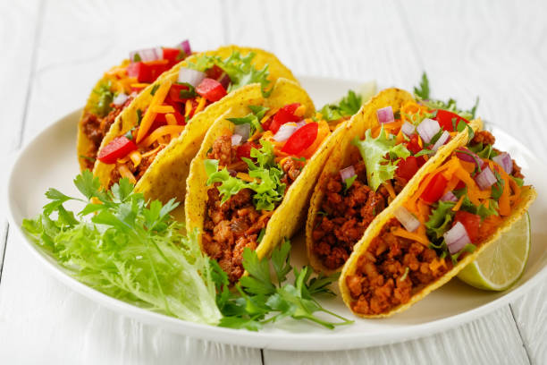 istock Ground Beef Tacos with shredded cheddar cheese, fresh lettuce, tomato, onion on a white plate with lime wedges, horizontal view from above, mexican cuisine 1337003258