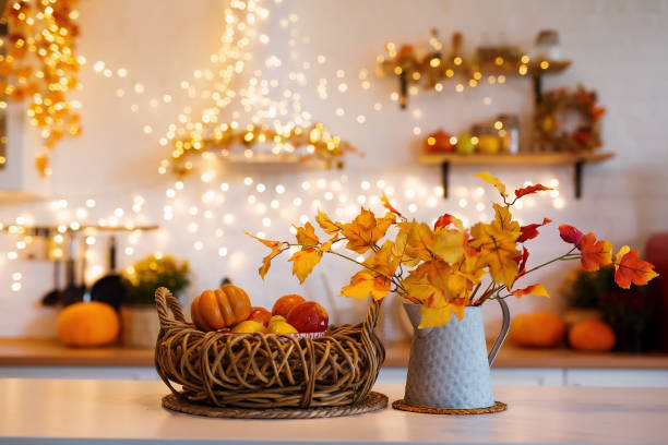 autumn kitchen interior. red and yellow leaves and flowers in the vase and pumpkin on light background - decoraties stockfoto's en -beelden