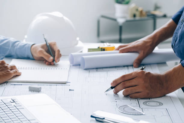 istock Two Architect discussing a project and working on blueprint at the construction site at desk in the office, Architectural and engineering concept. 1337011819
