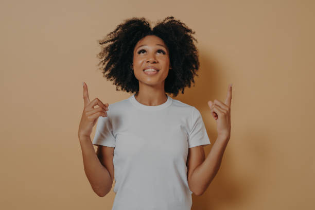 istock Curly african woman pointing with forefingers upwards at copy space against brown studio wall 1337016204
