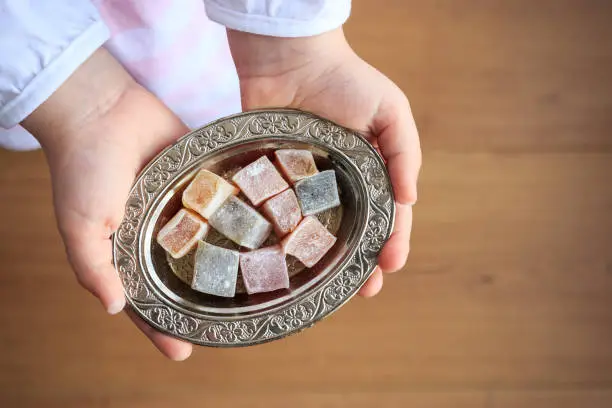 Photo of Top view of colorful Turkish delight in silver bowl on the little girl hands. Traditional ramadan holiday in Turkey. Turkish culture concept.