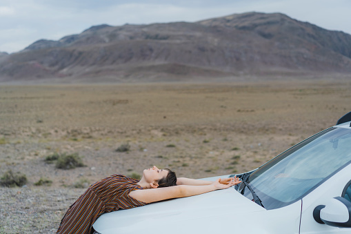 Young Caucasian woman laying on the car in the desert