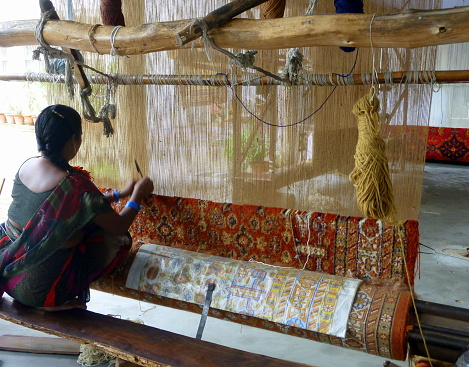 Rear view of an unrecognizable woman at the loom for weaving a typical carpet, Jaipur, India