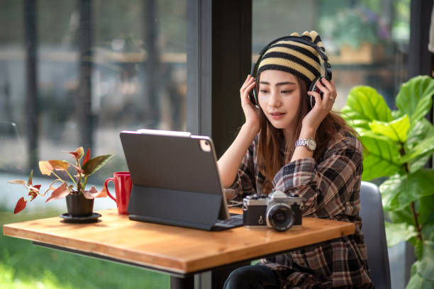 istock Image of an Asian woman student wearing headphones and learning using a tablet camera placed at a café table. 1337028767