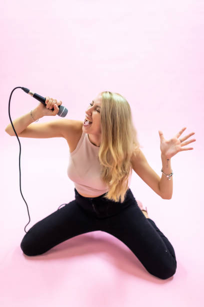 istock Beautiful young woman with microphone singing on pink background 1337029726