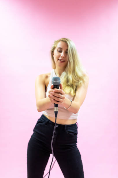 istock Beautiful young woman with microphone singing on pink background 1337029740