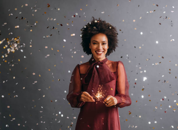 czas świętować: portret pięknej afroamerykanki trzymającej noworoczny zraszacz w deszczu konfetti (szare tło) - party frock zdjęcia i obrazy z banku zdjęć