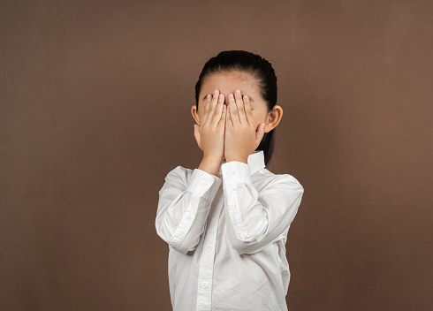 Little Girl Hands Covering Face on Brown Background