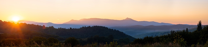 Beautiful panoramic mountain landscape with hazy peaks and foggy valley at sunset.