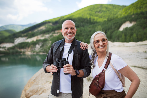 A happy senior couple on hiking trip on summer holiday, using binoculars.