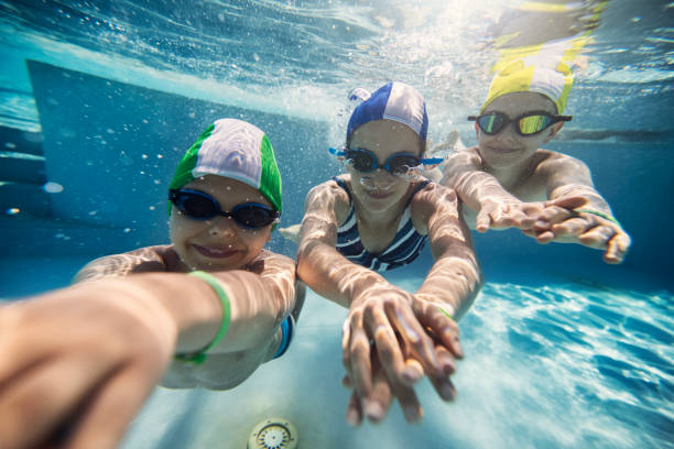 drei glückliche kinder schwimmen unter wasser im pool - bademütze stock-fotos und bilder