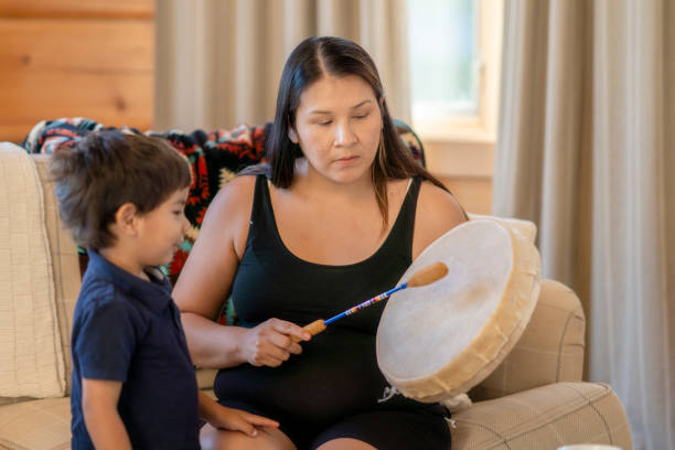 Indigenous mother playing the drums for her son at home A young Indigenous mother  is playing a traditional drum for her son at home. She is sharing her family's tradition and culture with her child. canadian culture stock pictures, royalty-free photos & images