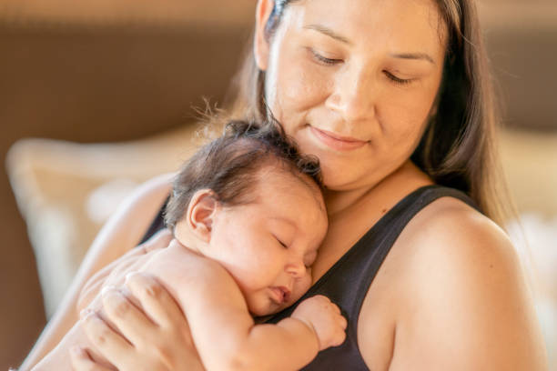 Cute baby girl sleeping on her mother's chest An adorable photo of a three (3) month old baby girl sleeping on her mother's chest. Her mother is looking down at her baby daughter with a soft smile on her face. canadian culture photos stock pictures, royalty-free photos & images
