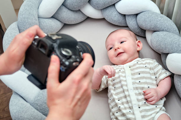 un fotógrafo toma fotos de un bebé recién nacido con una cámara en la cuna. sesión de fotos de niños en el interior del hogar - bebé fotos fotografías e imágenes de stock