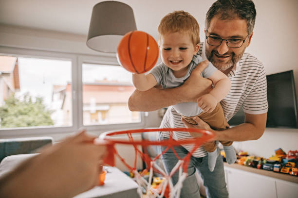 Father and son having fun, playing basketball at home Photo of happy little boy playing basketball  with his parents at home toddler hitting stock pictures, royalty-free photos & images