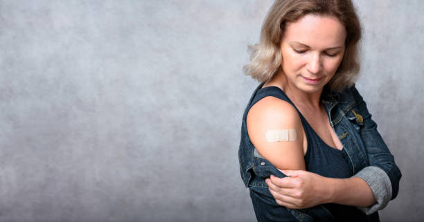 istock Vaccinated young woman showing arm with plaster on gray wall background 1337062863